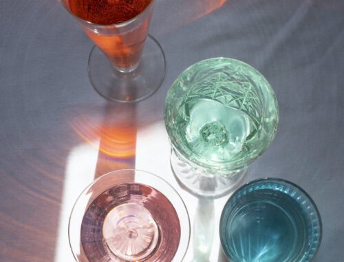 From above of crystal glasses filled with refreshing drinks on white table in sunlight