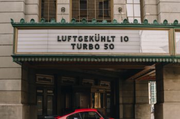 A red car parked in front of a movie theater