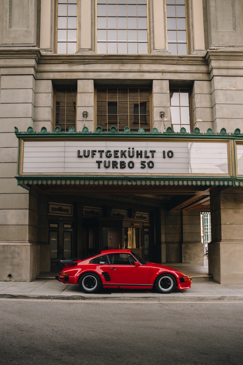 A red car parked in front of a movie theater